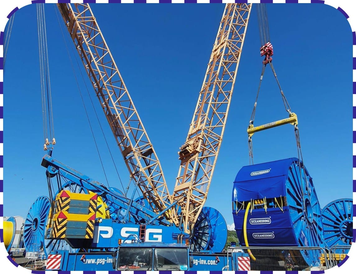 A crane lifts a large blue machine at a construction site